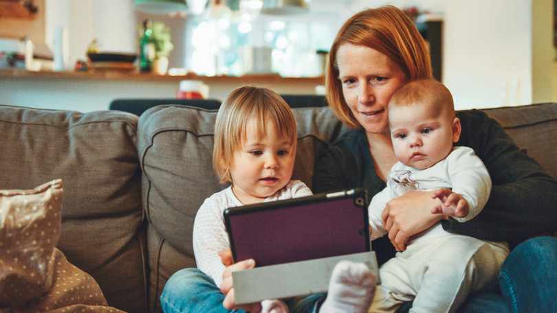 Eine Mutter guckt auf der Couch zu Hause mit ihren Kinder auf ein Tablet