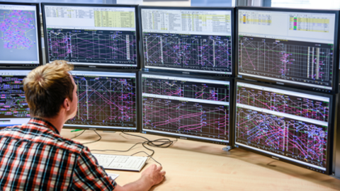 Ein Mitarbeiter sitzt vor acht Bildschirmen und blickt auf komplexe Daten und Grafiken