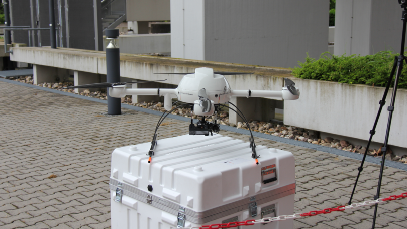 Eine weiße Multikopter-Drohne steht auf einer weißen Platik-Box.