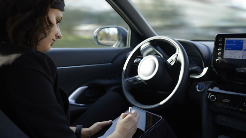 Eine Frau sitzt am Steuer und bedient während der Fahrt ein Tablet