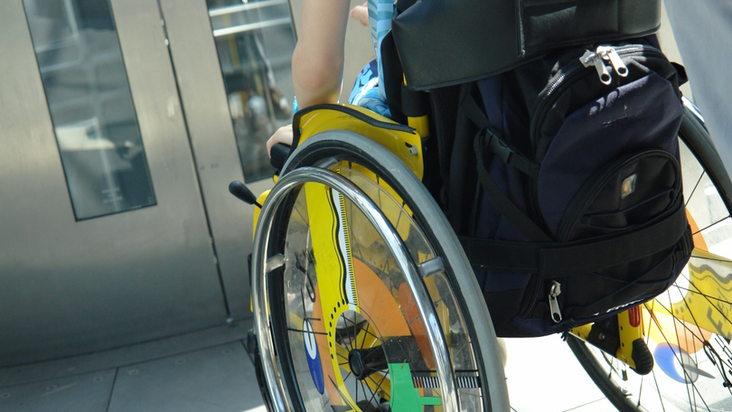 Eine Person im Rollstuhl wartet vor einem Aufzug