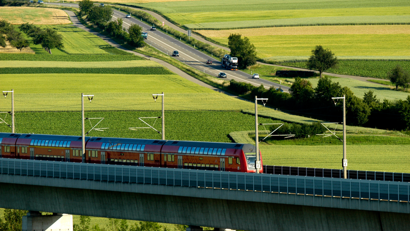 Landschaftsfoto mit einer fahrenden Eisenbahn und einer Straße im Hintergrund