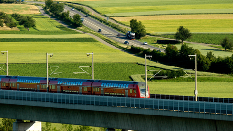 Landschaftsfoto mit einer fahrenden Eisenbahn und einer Straße im Hintergrund