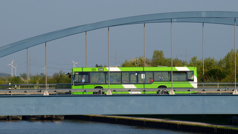 Grüner Bus auf Brücke über einem Fluss