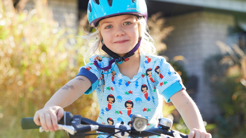 Ein Kind mit Fahrradhelm sitzt auf einem Fahrrad und blickt lächelnd in die Kamera