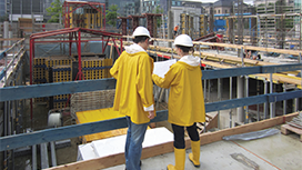 Zwei Personen mit Helm lesen einen Plan auf einer Baustelle